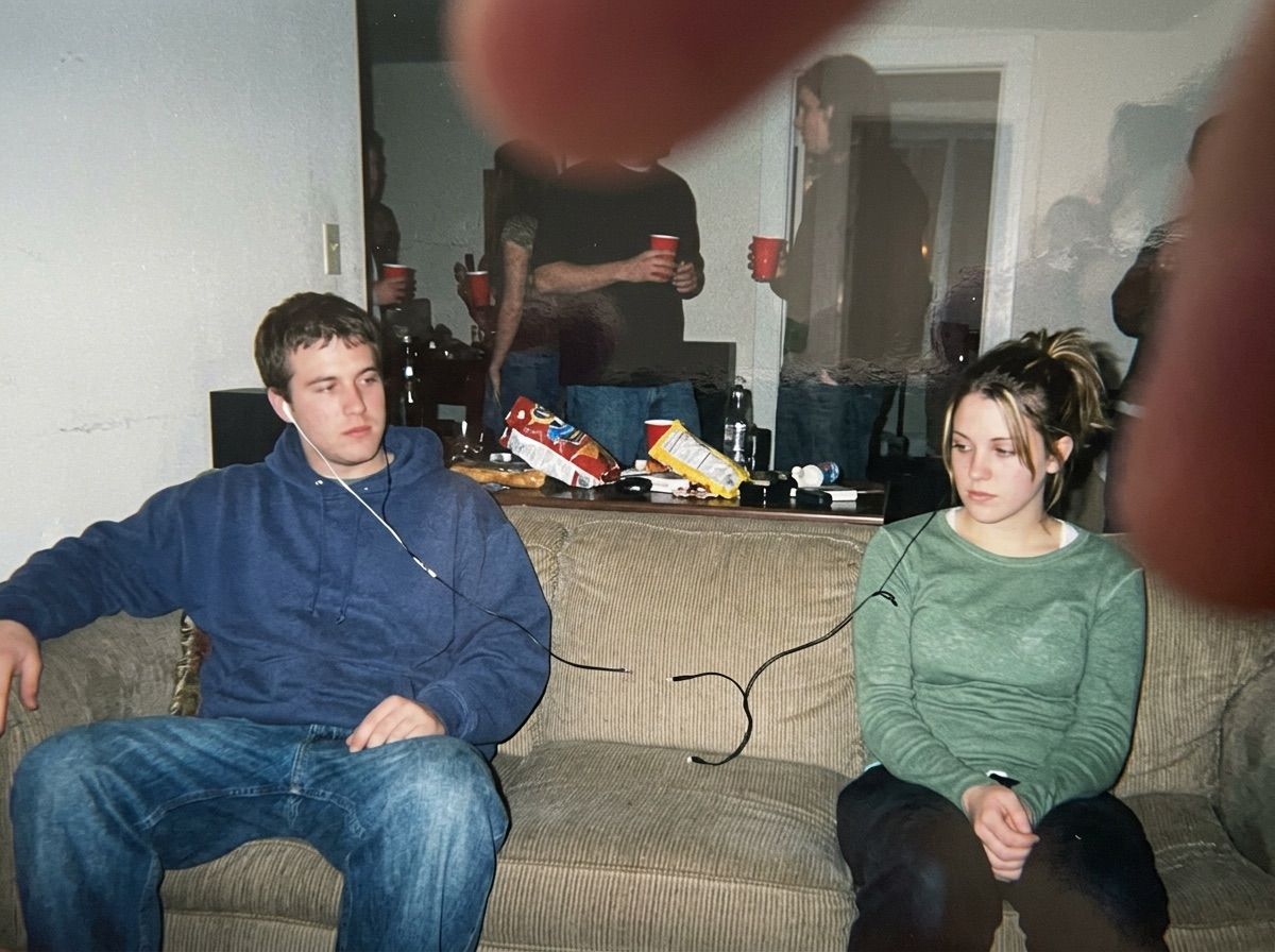 Two people on a sofa share wired earphones whose cable is visibly snapped in the middle