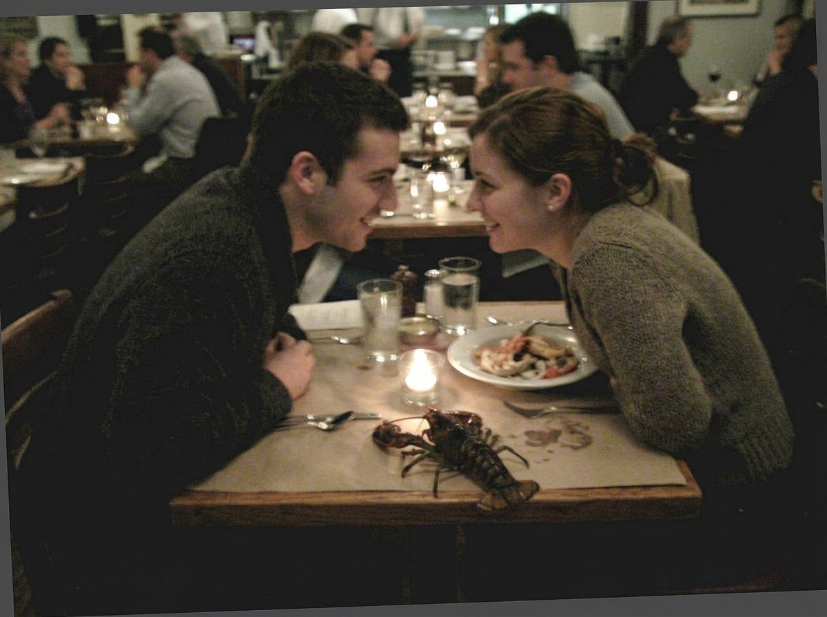 A couple lean in on a date while a lobster walks across the table between them
