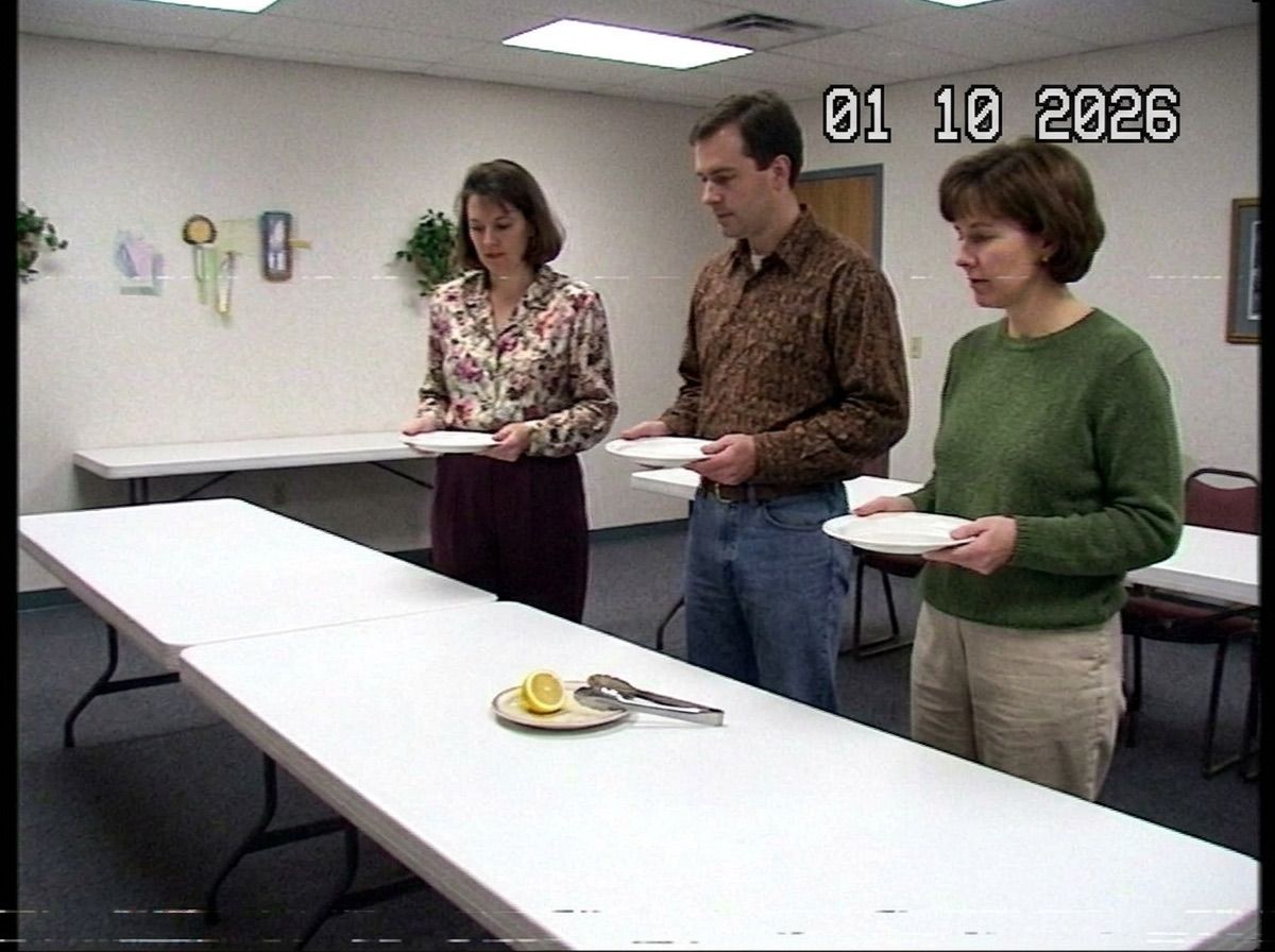 Three people with empty plates wait at a buffet table holding only a lemon slice and tongs