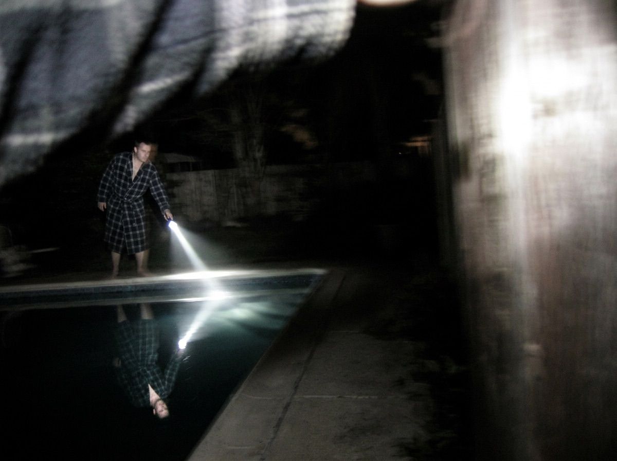 A man shines a torch into a dark pool at night and sees only his own reflection