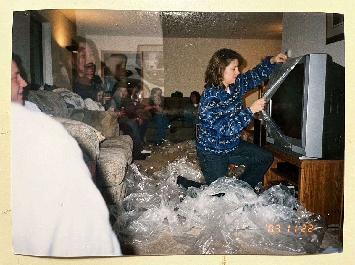 A woman peels film from a new TV while knee-deep in film she has already removed