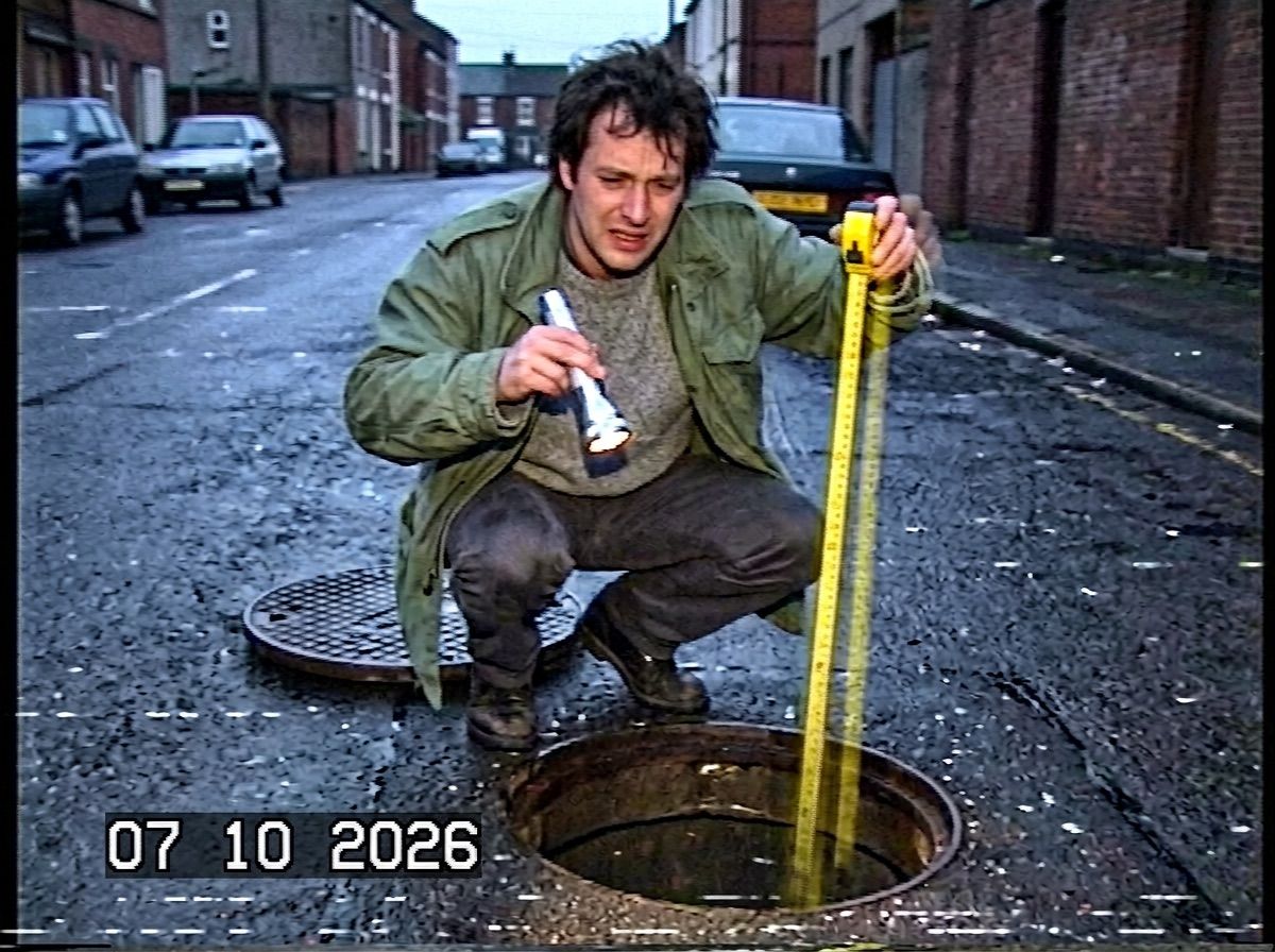 A man lowers a fully extended short tape measure into an open manhole