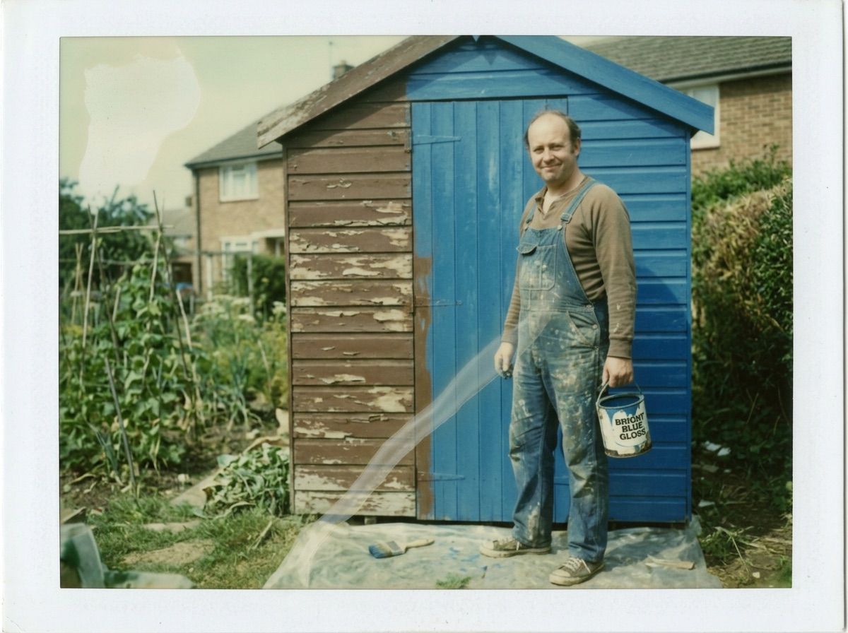 A man stands proudly by a shed painted blue on one half and flaking brown on the other