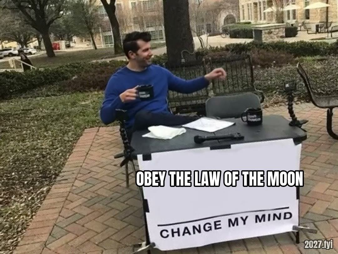 A man at a table with a sign: OBEY THE LAW OF THE MOON, CHANGE MY MIND